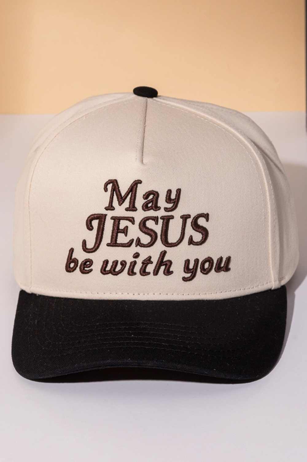 Black Classic two-tone trucker cap featuring an embroidered "MAY JESUS BE WITH YOU" message across the front. Crafted from 100% cotton for breathability and comfort, this snapback design offers one-size-fits-most versatility. Perfect for everyday wear, outdoor activities, or expressing your faith. The structured six-panel construction and mesh back panels provide durability and ventilation. An ideal accessory for those seeking meaningful style with spiritual significance.