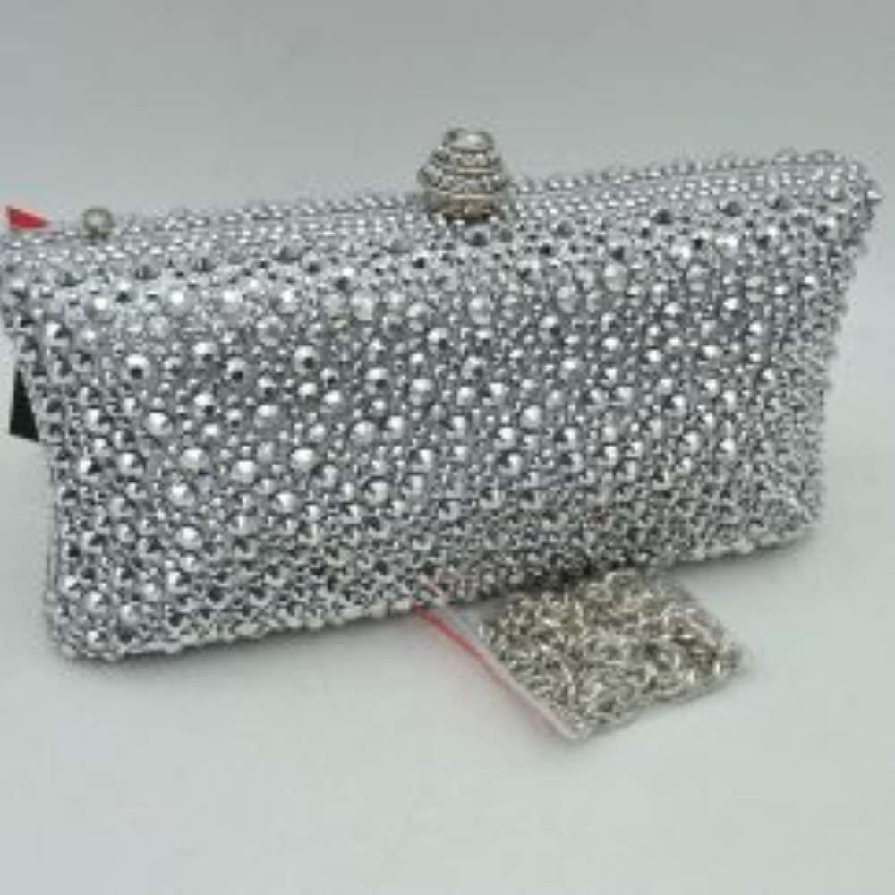 Silver This elegant box clutch bag features an all-over array of faceted, shimmering rhinestone embellishments that fully cover the exterior for a textured, light-catching look. Designed for evening or special occasion use, the structured frame includes a secure top clasp closure with a tiered, decorative knob that easily snaps open to access the main storage compartment. A matching, detachable metallic link chain strap with a secure lobster clasp is included