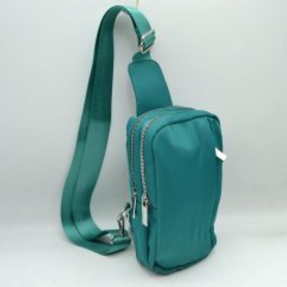 Teal This functional sling bag features a smooth, clean exterior w/ a structured vertical silhouette designed for active everyday use. It offers multiple organized storage compartments, including a primary back section and a secondary front pocket, both accessed via parallel top-curved zipper tracks w/ sleek metallic pulls. The bag is equipped w/ a wide, woven fabric shoulder strap attached to a integrated top panel and secured w/ an adjustable metallic buckle to easily customize the carrying length.