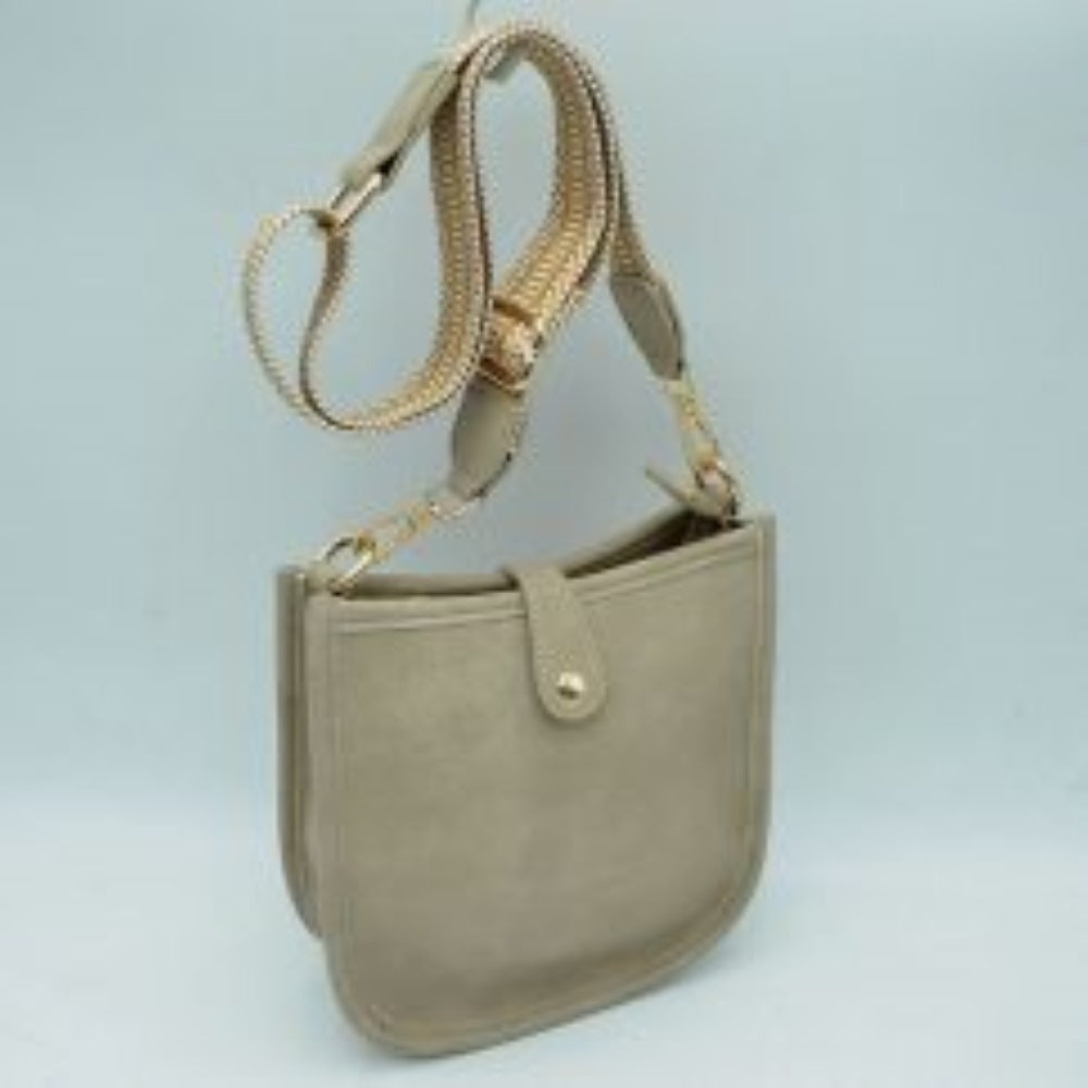 Beige This stylish crossbody bag presents a clean, minimalist design with a smooth exterior finish and a distinct curved, U-shaped silhouette perfect for everyday use. It features an open top main compartment equipped with a small secure tab closure that fastens at the front with a metallic snap button. Adding a striking contrast, the bag is paired with a thick, adjustable fabric strap showcasing a bold geometric pattern