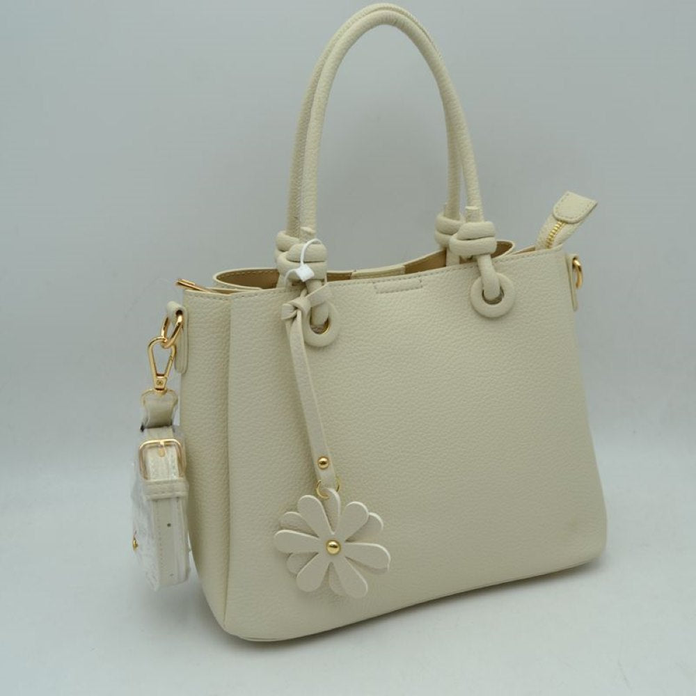 Beige This elegant everyday bag features a textured surface and unique rolled top handles that attach to the body with knotted loop accents. The design offers versatile storage options, highlighting a split-compartment interior with an open side section and a main central area secured by a metallic top zipper. A decorative floral charm hangs from the front handle base, and a detachable, adjustable shoulder strap is connected via metallic lobster clasps to side D-rings