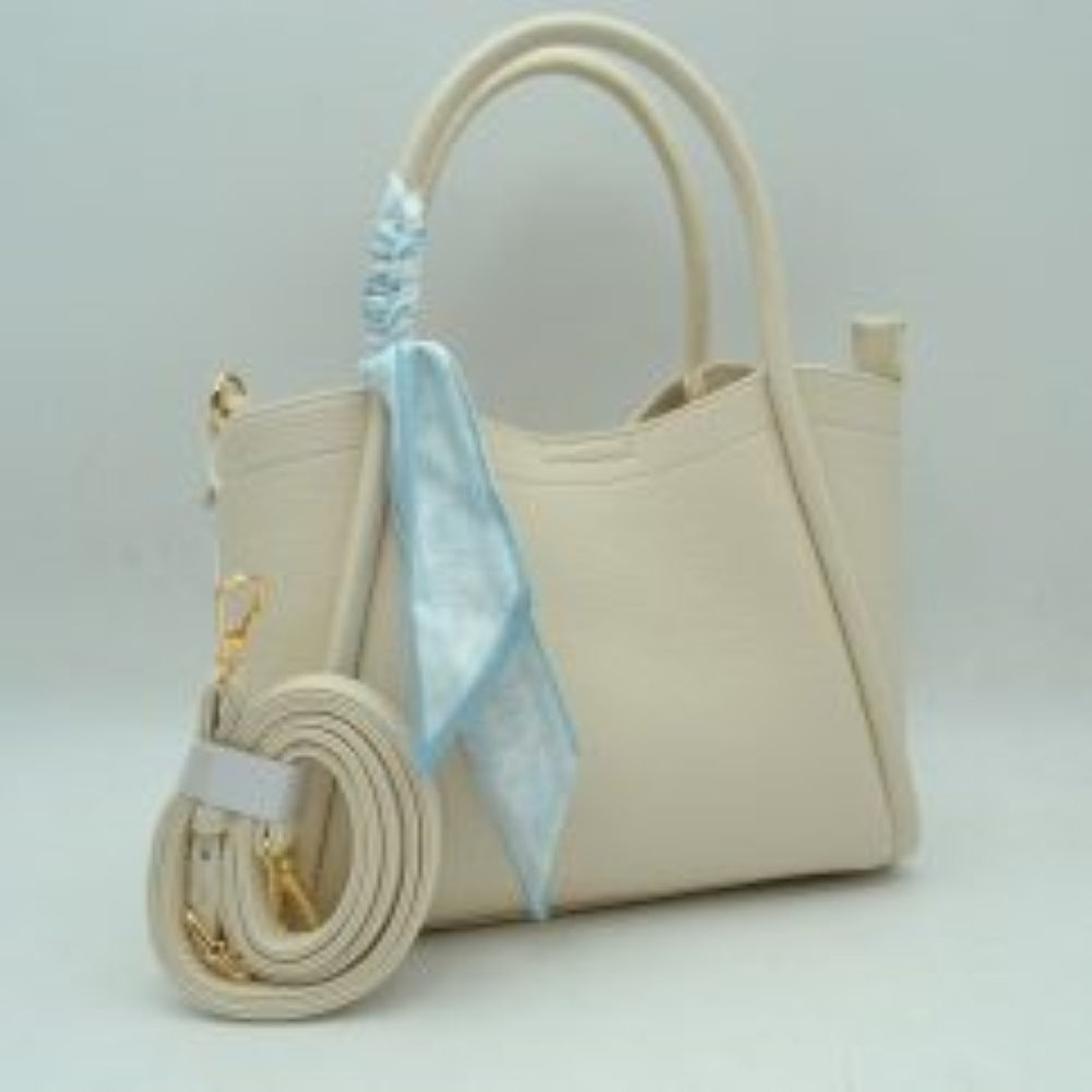 Bige This structured handbag features dual top handles and a subtle curved topline design, complemented by a decorative patterned scarf wrapped around one handle base. It includes an adjustable, detachable shoulder strap with gold-toned metal hardware that clips onto side rings, offering multiple carrying options for everyday use.