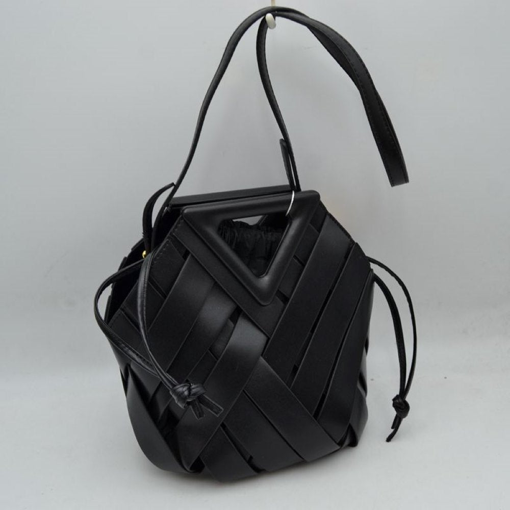 Black This structural bucket bag features a distinctive geometric design composed of overlapping wide woven straps that create an eye-catching pattern, making it a unique statement piece for everyday use. A rigid triangular cutout shape forms an integrated top handle, while an additional long, flat shoulder strap extends from the upper frame for comfortable over-the-shoulder carrying.