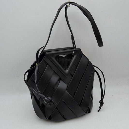 Black This structural bucket bag features a distinctive geometric design composed of overlapping wide woven straps that create an eye-catching pattern, making it a unique statement piece for everyday use. A rigid triangular cutout shape forms an integrated top handle, while an additional long, flat shoulder strap extends from the upper frame for comfortable over-the-shoulder carrying.