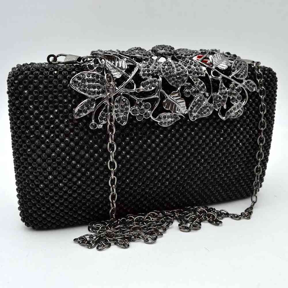 Black Designed with a rigid rectangular silhouette, this sophisticated box clutch features a meticulously textured exterior composed of small, shimmering circular studs arranged in a uniform pattern. A detailed overlay consisting of metallic leaves and floral accents spans across the top closure, creating an elegant focal point while securing the main storage compartment. A matching link chain strap attaches seamlessly to the top edges