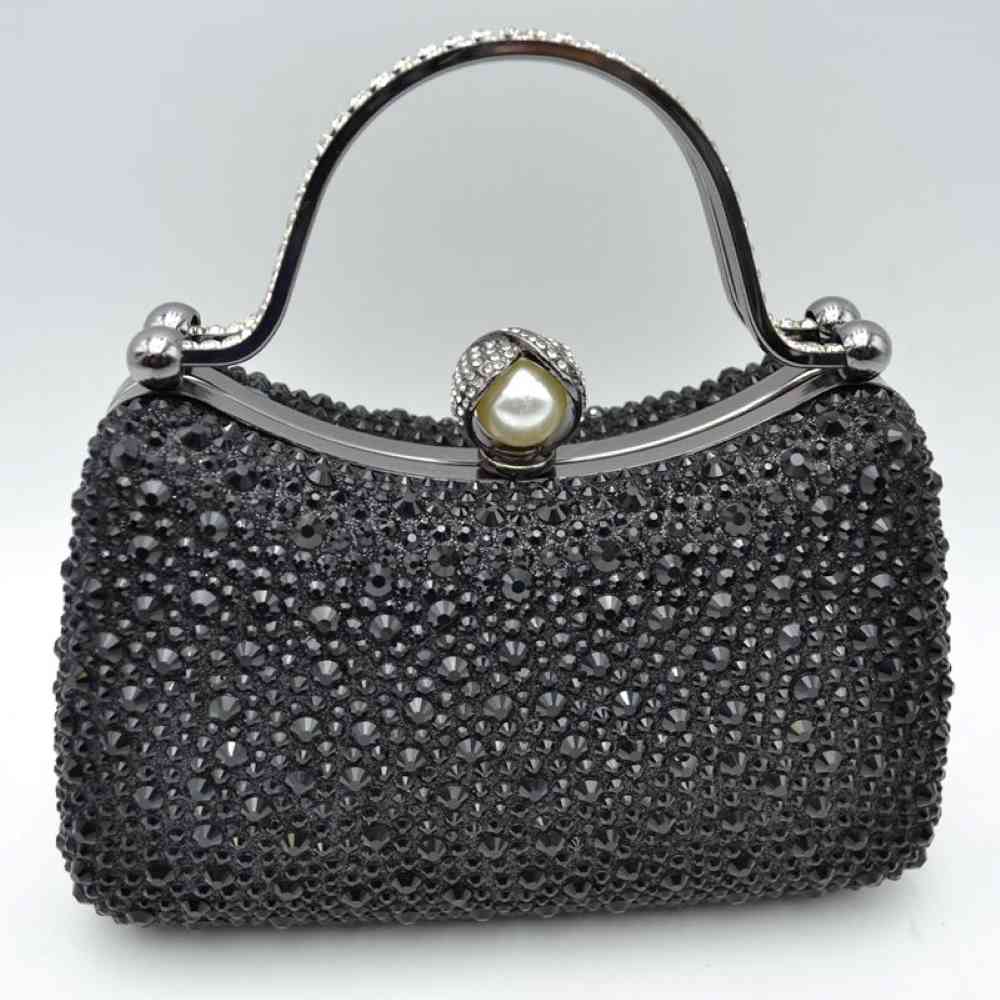 Black This elegant evening clutch bag features a structured silhouette heavily encrusted with shimmering black rhinestones, offering a highly textured and glamorous look for formal events. A sleek, curved metallic top handle lined with delicate crystals rises over the frame for a secure grip, anchored by polished spherical accents. The secure metal frame is highlighted by a prominent decorative clasp featuring a large faux pearl wrapped in rhinestone-studded detailing