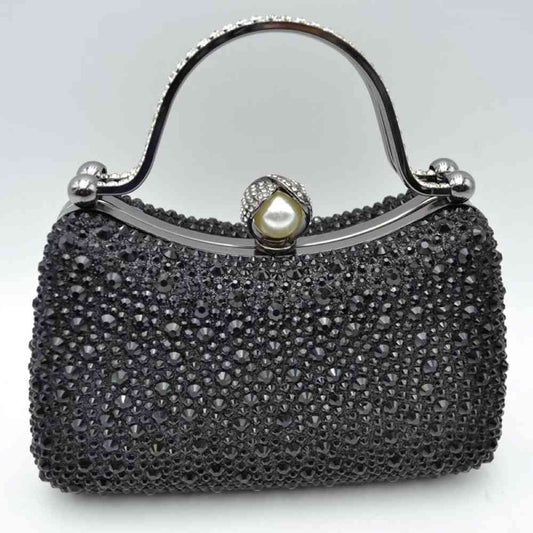 Black This elegant evening clutch bag features a structured silhouette heavily encrusted with shimmering black rhinestones, offering a highly textured and glamorous look for formal events. A sleek, curved metallic top handle lined with delicate crystals rises over the frame for a secure grip, anchored by polished spherical accents. The secure metal frame is highlighted by a prominent decorative clasp featuring a large faux pearl wrapped in rhinestone-studded detailing
