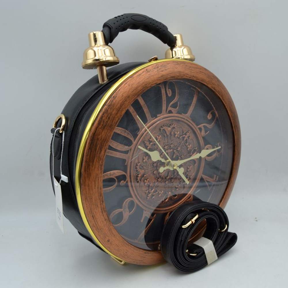 Black This unique novelty handbag features a structured round silhouette designed to look like a vintage twin-bell alarm clock, making it an exceptional statement piece. The prominent front panel showcases a large clock face detailed with oversized numbers and ornate gold-tone hands, beautifully enclosed within a wood-grain textured circular frame and a clear protective cover. Mimicking a classic alarm clock