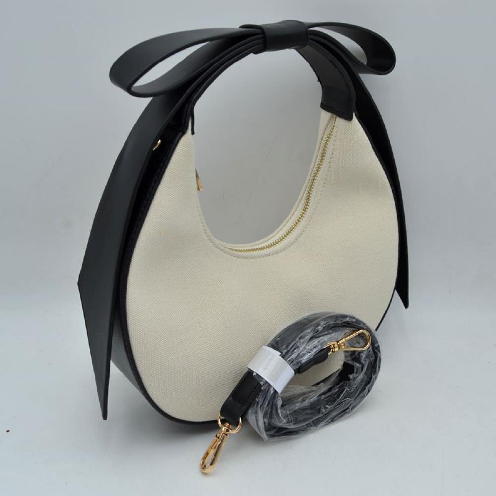 Black Add a touch of feminine charm to your accessory collection with this striking crescent-shaped hobo bag. Blending the natural texture of a heavy-duty canvas body with an architectural, oversized bow handle, this statement handbag effortlessly bridges the gap between playful romance and contemporary high fashion. Whether worn as a chic top-handle bag or converted into a hands-free crossbody, its unique silhouette makes it a standout piece for any outfit.