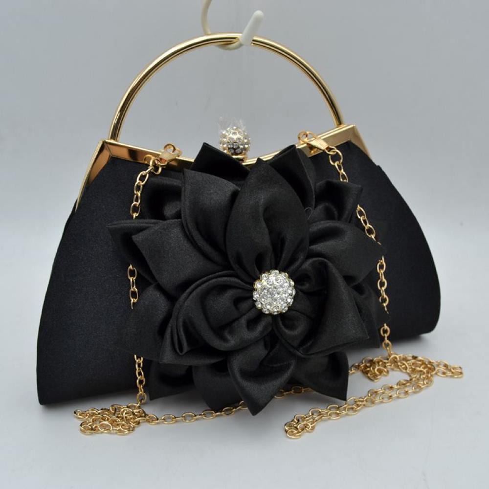Black This elegant evening clutch bag features a smooth, structured body dominated by a large, multi-layered fabric flower accent right on the front panel. Designed for special events and everyday formal use, the main storage compartment is secured by a metal frame top with a shimmering, rhinestone-embellished clasp closure.
