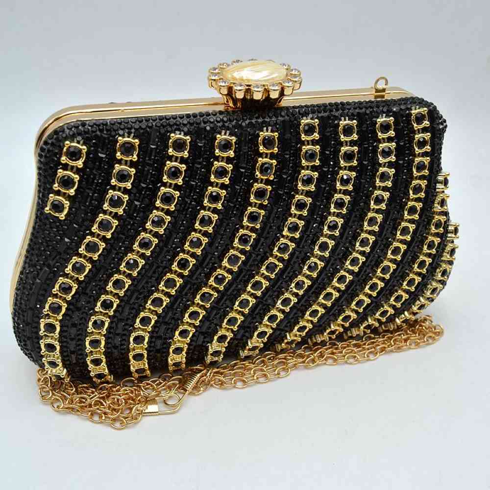 Black This luxurious evening clutch bag features a hard-shell structured body completely embellished with shimmering black rhinestones and crystals. The striking design is accented by elegant, wavy diagonal stripes of gold-toned settings framing black round stones across the front panel. Ideal for formal gatherings, weddings, or special galas, the main compartment is secured by a polished gold-toned top frame with an ornate, jewel-encrusted crown clasp closure.