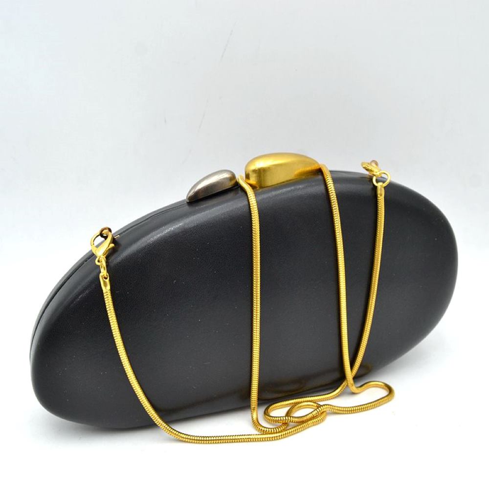 Black This structured hardcase clutch bag features a smooth, rounded oval silhouette designed as a sleek accessory for everyday use. Its single interior storage compartment is secured with a rigid frame closure, accented at the top by a distinctive, asymmetrical two-tone sculptural clasp. A slender, matching metallic snake chain strap connects to small loop anchors on either side via clasp attachments, offering convenient options for hands-free shoulder or crossbody styling.