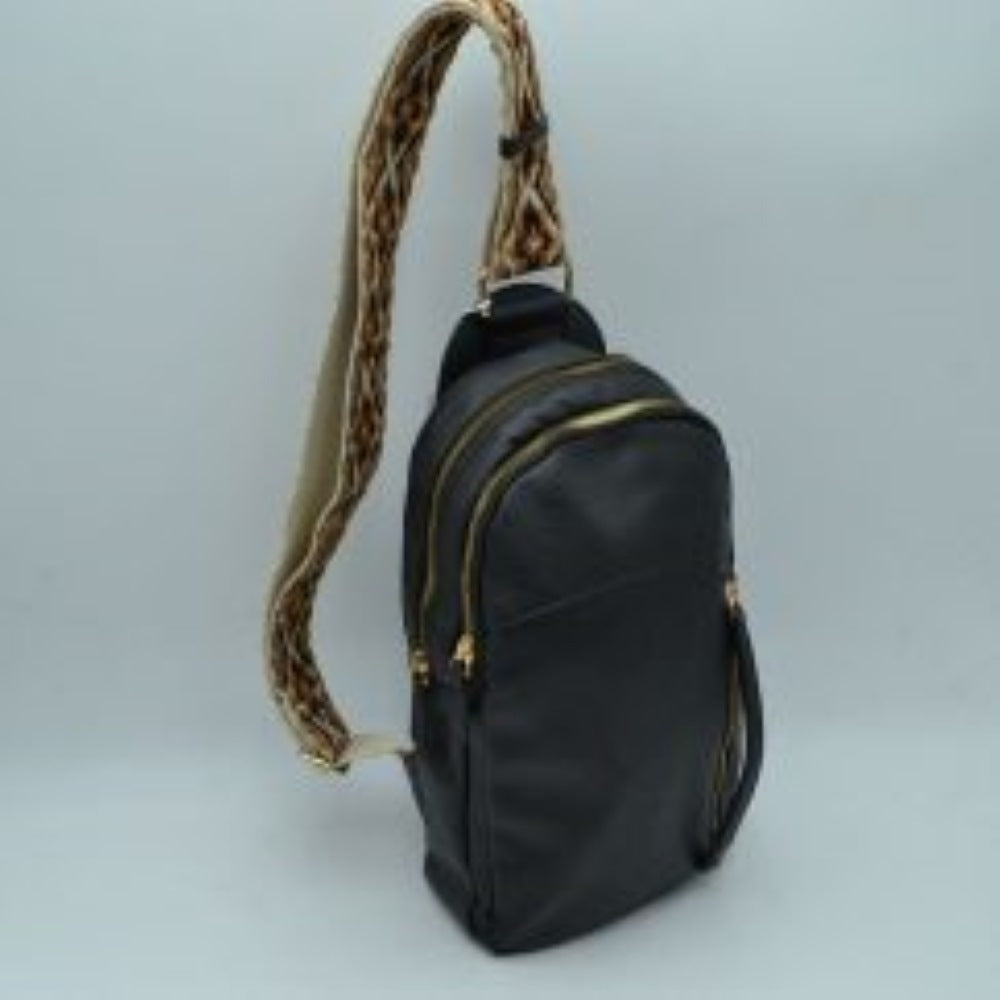 Black This multi-compartment sling backpack features a smooth texture and a contoured, upright silhouette optimized for daily use. It offers practical storage compartments, consisting of two tiered main sections with independent gold-tone zipper closures alongside a side-access vertical zippered pocket. A distinctive, wide fabric shoulder strap decorated with a detailed geometric woven pattern connects securely to the top and bottom anchors