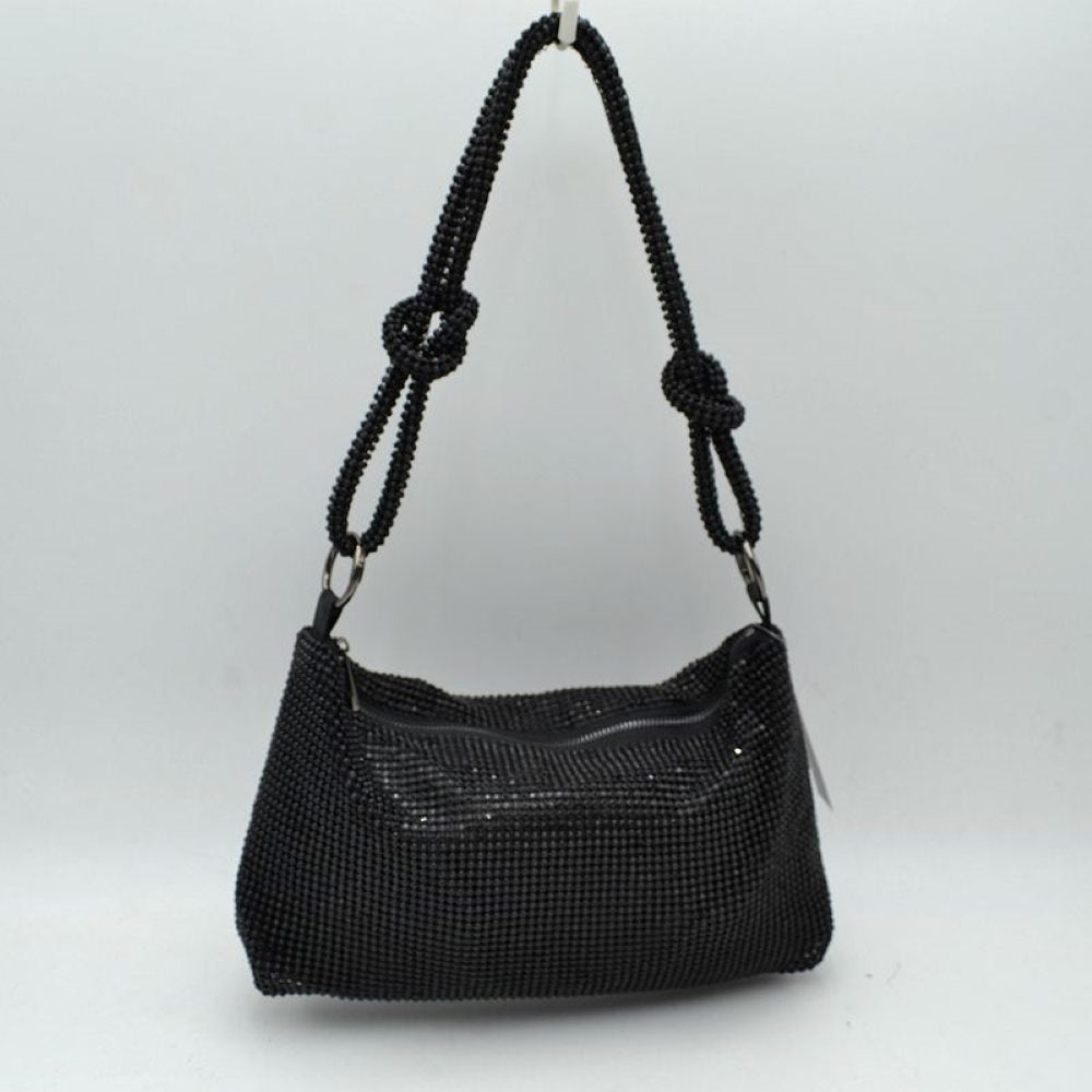 Black This shoulder bag features a textured grid exterior suitable for versatile everyday use. It includes a main storage compartment accessible via a top zipper closure to keep personal items secure. The bag is completed by a matching textured shoulder strap that features integrated decorative knots on each side and connects to the main body through circular rings.
