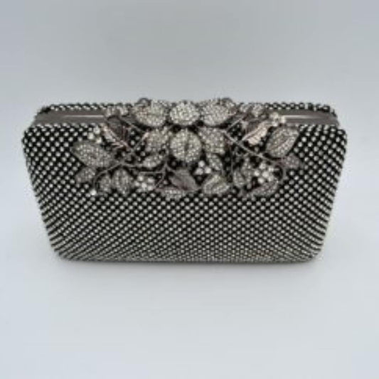 Black Designed with a rigid rectangular silhouette, this sophisticated box clutch features a meticulously textured exterior composed of small, shimmering circular studs arranged in a uniform pattern. A detailed overlay consisting of metallic leaves and floral accents spans across the top closure, creating an elegant focal point while securing the main storage compartment. A matching link chain strap attaches seamlessly to the top edges