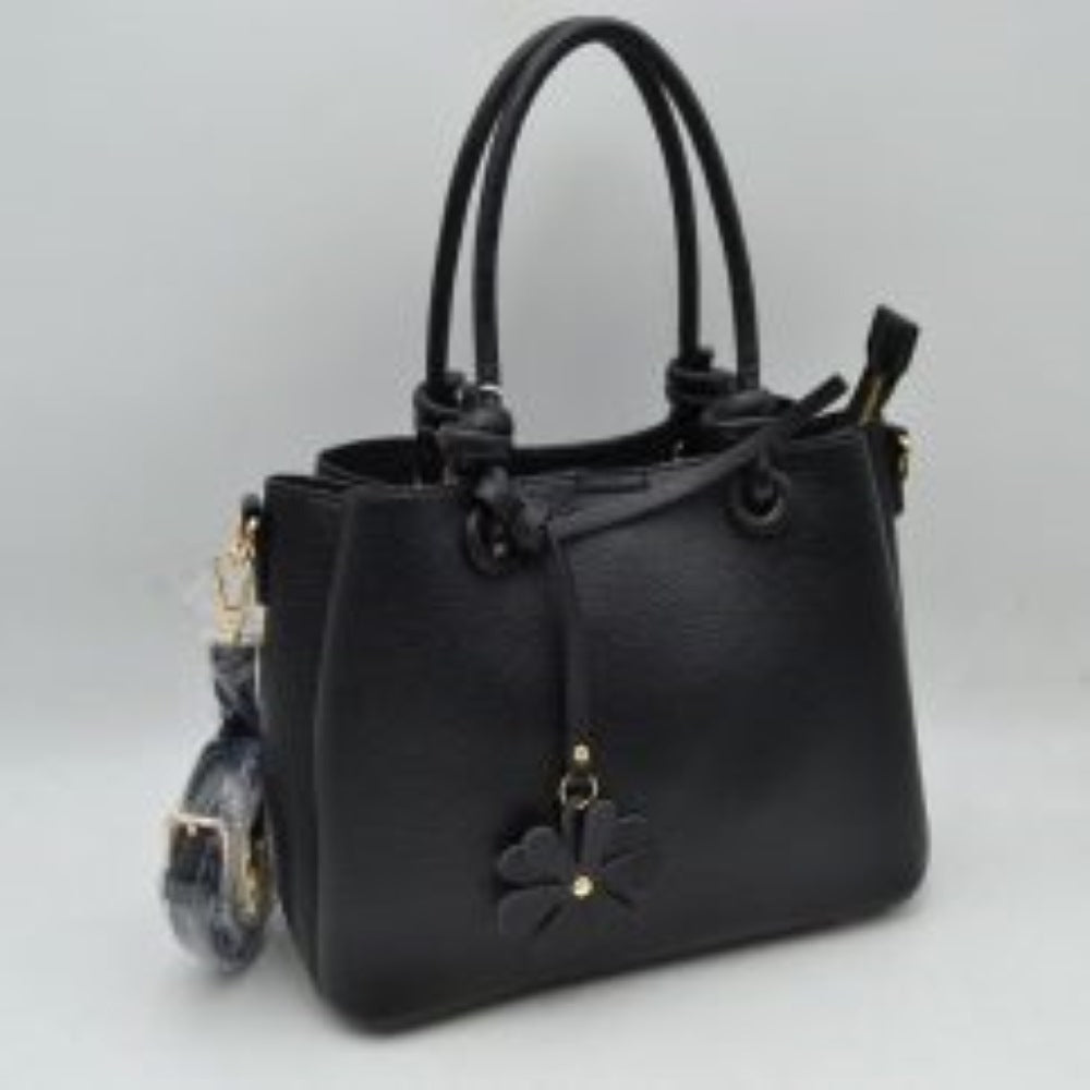 Black This elegant everyday bag features a textured surface and unique rolled top handles that attach to the body with knotted loop accents. The design offers versatile storage options, highlighting a split-compartment interior with an open side section and a main central area secured by a metallic top zipper. A decorative floral charm hangs from the front handle base, and a detachable, adjustable shoulder strap is connected via metallic lobster clasps to side D-rings