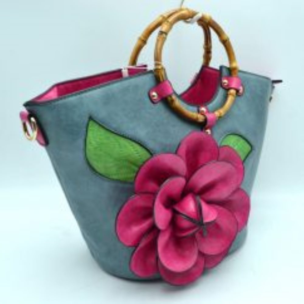 Blue This structural tote bag is designed for standout everyday use, showcasing a prominent three-dimensional floral applique paired with stitched leaf accents on the front panel. It features segmented, circular top handles secured to the curved upper rim with studded contrasting tabs. The main storage compartment opens widely at the top to reveal a vibrant interior lining