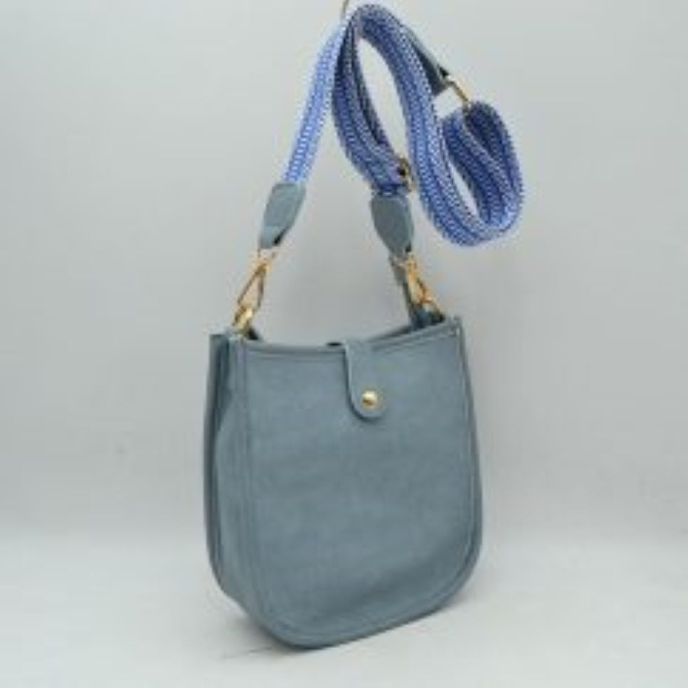 Blue This stylish crossbody bag presents a clean, minimalist design with a smooth exterior finish and a distinct curved, U-shaped silhouette perfect for everyday use. It features an open top main compartment equipped with a small secure tab closure that fastens at the front with a metallic snap button. Adding a striking contrast, the bag is paired with a thick, adjustable fabric strap showcasing a bold geometric pattern