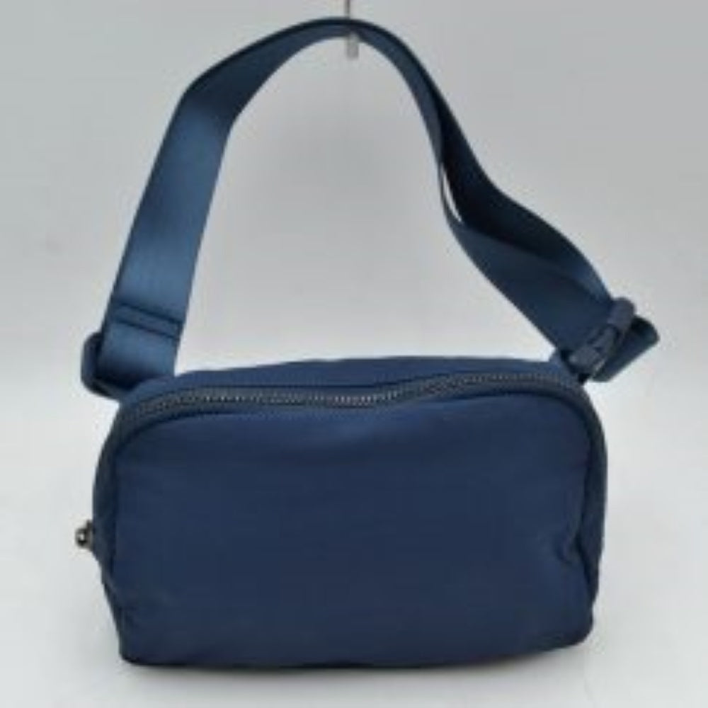 Blue This minimalist bag features a smooth, clean design ideal for versatile everyday use. The main storage compartment is secured by a curved top zipper with dual pulls for easy access to essentials. A wide, adjustable strap extends from the sides, complete with a matching slider to easily customize the fit for comfortable carrying.