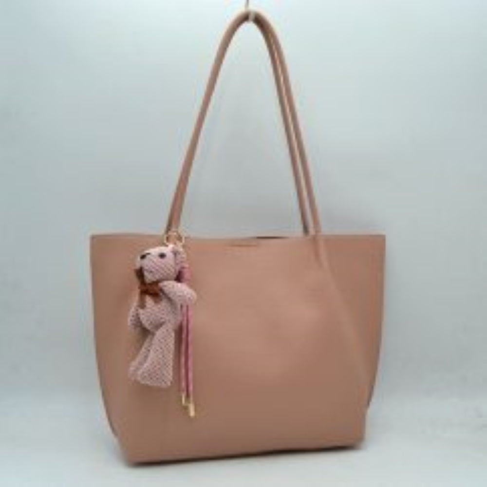 Blush his classic tote bag features a subtly pebbled exterior texture with a relaxed yet structured silhouette that is ideal for everyday use. Designed with a clean, open top for convenient access to the spacious main storage compartment, the bag is equipped with dual long, slim shoulder handles securely anchored to the interior panels. A decorative plush bear charm with a tiny bow sits on the front