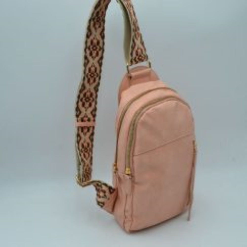 Blush This multi-compartment sling backpack features a smooth texture and a contoured, upright silhouette optimized for daily use. It offers practical storage compartments, consisting of two tiered main sections with independent gold-tone zipper closures alongside a side-access vertical zippered pocket. A distinctive, wide fabric shoulder strap decorated with a detailed geometric woven pattern connects securely to the top and bottom anchors