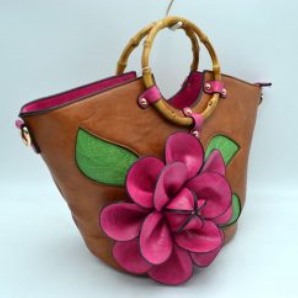 Brown This structural tote bag is designed for standout everyday use, showcasing a prominent three-dimensional floral applique paired with stitched leaf accents on the front panel. It features segmented, circular top handles secured to the curved upper rim with studded contrasting tabs. The main storage compartment opens widely at the top to reveal a vibrant interior lining