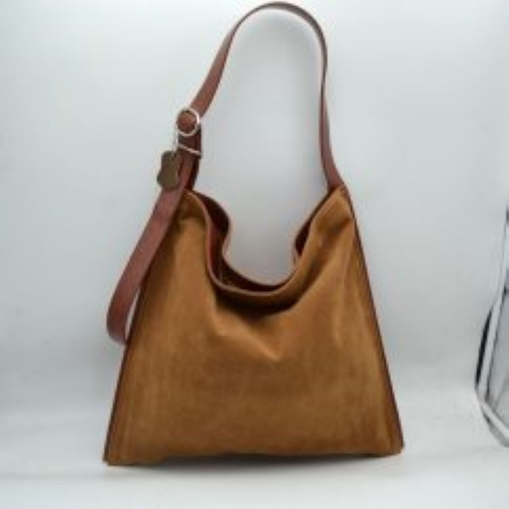 Brown This slouchy hobo bag features a clean, soft-textured exterior with a relaxed, square-shaped silhouette that makes it ideal for everyday use. Designed with a spacious main compartment to easily organize and store daily essentials, the bag is equipped with a wide, flat shoulder strap for comfortable carrying. The single strap includes a metallic buckle closure system on one side, allowing for functional adjustments while adding a touch of classic detail to the overall minimalist design.