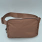 Brown This minimalist bag features a smooth, clean design ideal for versatile everyday use. The main storage compartment is secured by a curved top zipper with dual pulls for easy access to essentials. A wide, adjustable strap extends from the sides, complete with a matching slider to easily customize the fit for comfortable carrying.