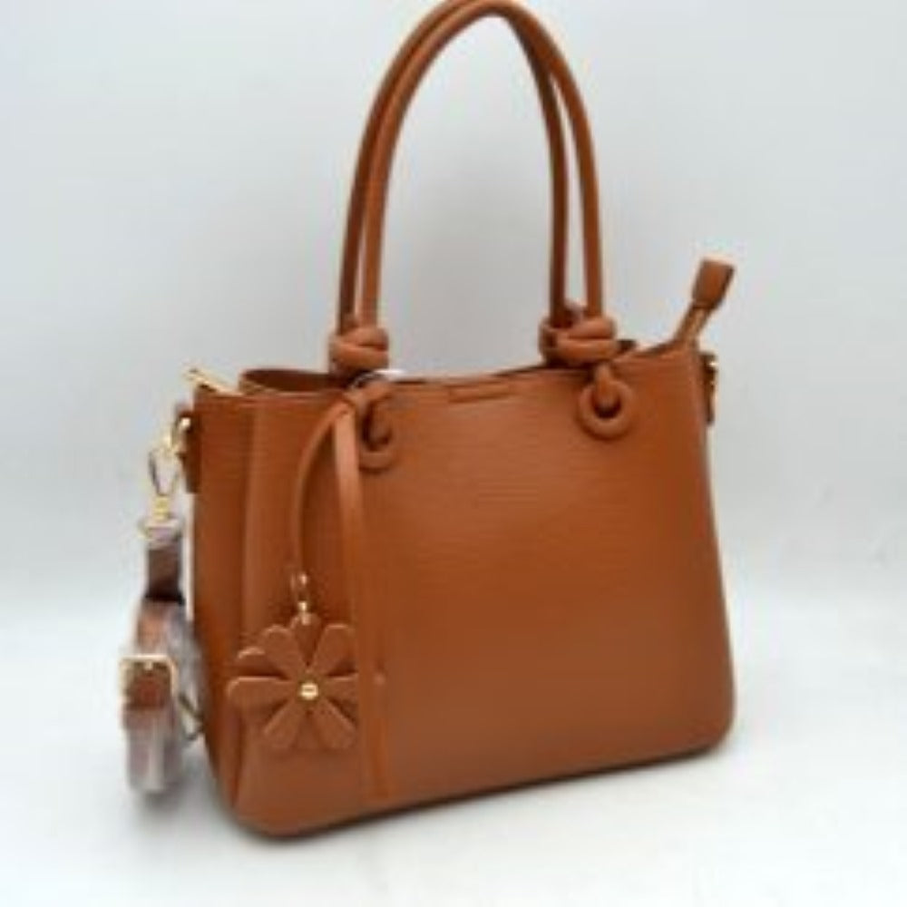 Brown This elegant everyday bag features a textured surface and unique rolled top handles that attach to the body with knotted loop accents. The design offers versatile storage options, highlighting a split-compartment interior with an open side section and a main central area secured by a metallic top zipper. A decorative floral charm hangs from the front handle base, and a detachable, adjustable shoulder strap is connected via metallic lobster clasps to side D-rings