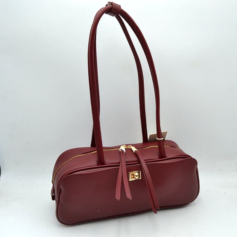 Burgundy This structured shoulder bag features a smooth, elongated silhouette with a clean exterior finish, making it an excellent choice for modern everyday use. The design stands out with long, rounded double top straps that loop over the main body for comfortable carrying on the shoulder or by hand. It is equipped with a secure top zipper closure featuring dual long pulls