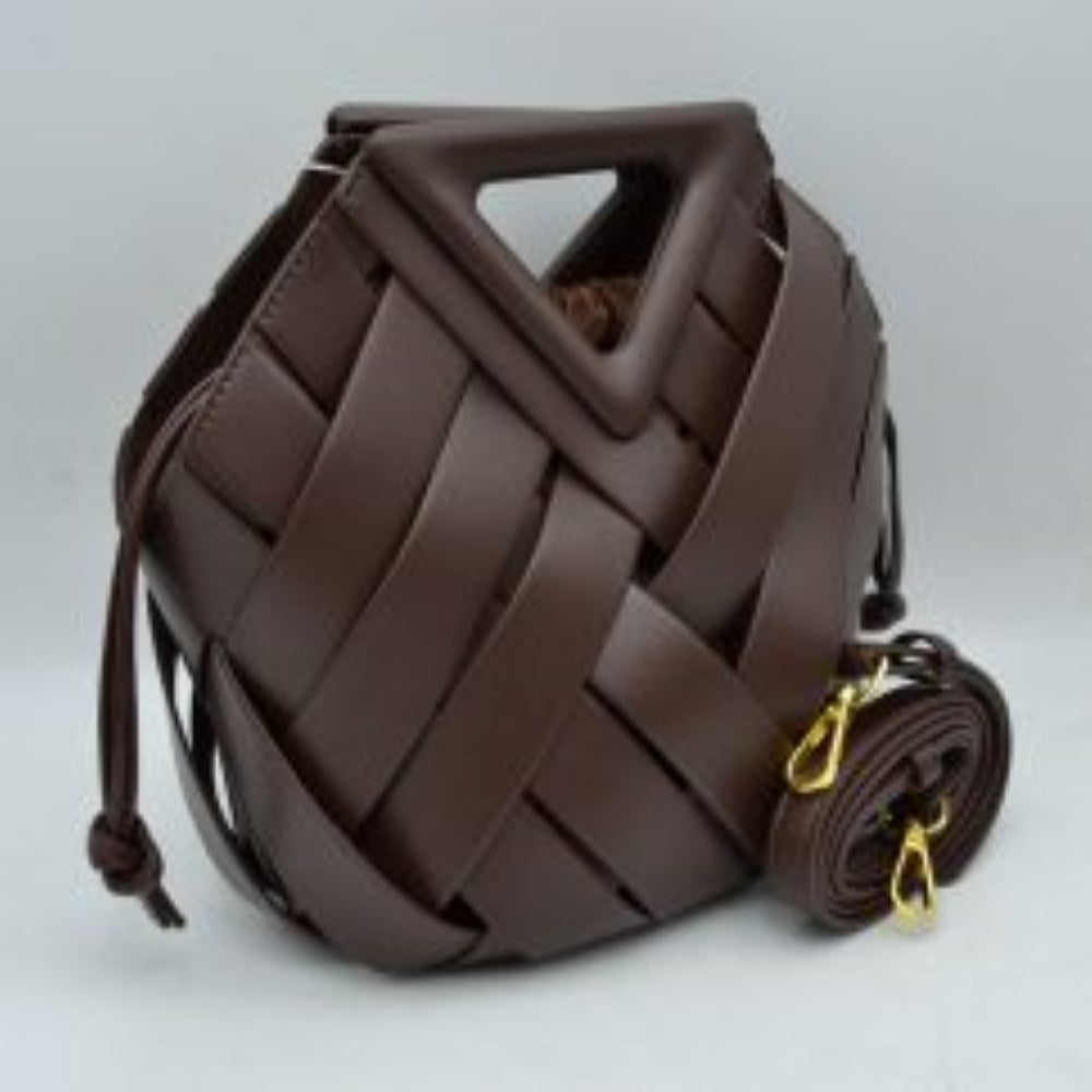 Coffee This structural bucket bag features a distinctive geometric design composed of overlapping wide woven straps that create an eye-catching pattern, making it a unique statement piece for everyday use. A rigid triangular cutout shape forms an integrated top handle, while an additional long, flat shoulder strap extends from the upper frame for comfortable over-the-shoulder carrying.