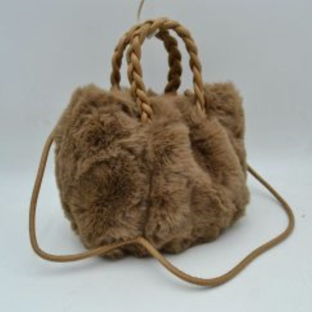 Coffee This soft everyday bucket-style handbag features a densely textured, plush exterior that offers a cozy aesthetic for daily use. Designed with a structured yet flexible silhouette, it features dual braided top handles for comfortable hand carrying alongside a slender, long shoulder strap that provides hands-free convenience. The top opening reveals a spacious central storage compartment ideal for organizing essential items