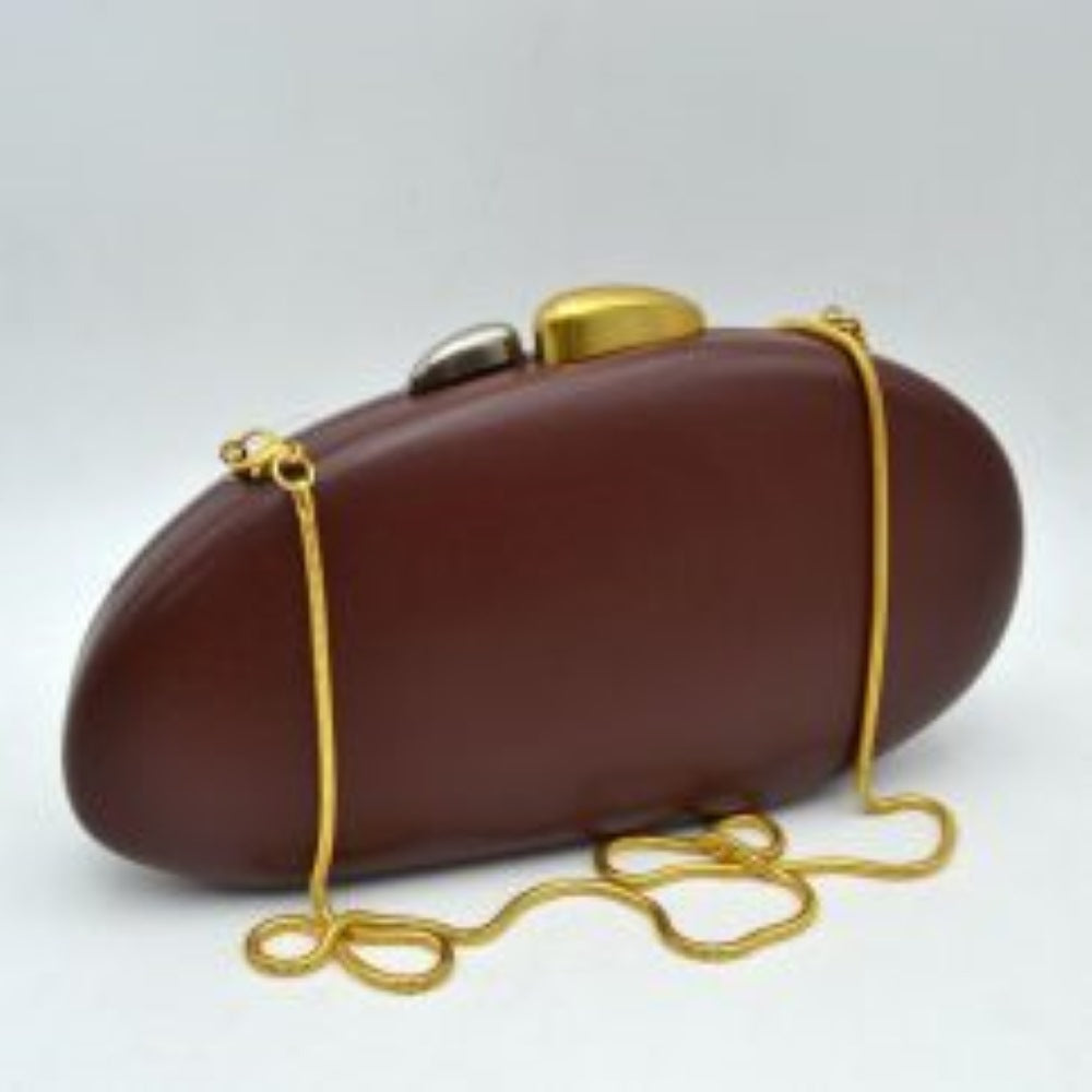 Coffee This structured hardcase clutch bag features a smooth, rounded oval silhouette designed as a sleek accessory for everyday use. Its single interior storage compartment is secured with a rigid frame closure, accented at the top by a distinctive, asymmetrical two-tone sculptural clasp. A slender, matching metallic snake chain strap connects to small loop anchors on either side via clasp attachments, offering convenient options for hands-free shoulder or crossbody styling.