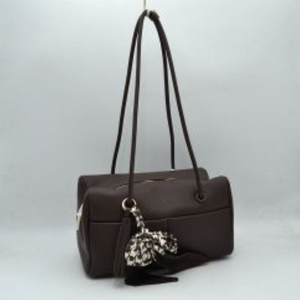 Coffee This structural shoulder bag features a textured pebbled exterior in a warm brown tone, offering a contemporary barrel-shaped silhouette for stylish everyday use. Designed with functionality in mind, it features dual long, slim shoulder straps that loop through metallic grommets directly into the body panels. The spacious main compartment opens with a secure top zipper closure, while a matching leather tassel and a patterned houndstooth fabric scarf tied around the front handle base add a playful