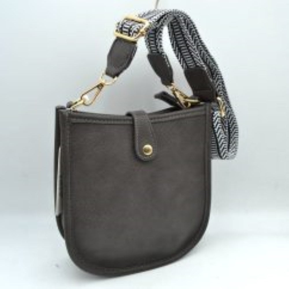Dark gray This stylish crossbody bag presents a clean, minimalist design with a smooth exterior finish and a distinct curved, U-shaped silhouette perfect for everyday use. It features an open top main compartment equipped with a small secure tab closure that fastens at the front with a metallic snap button. Adding a striking contrast, the bag is paired with a thick, adjustable fabric strap showcasing a bold geometric pattern