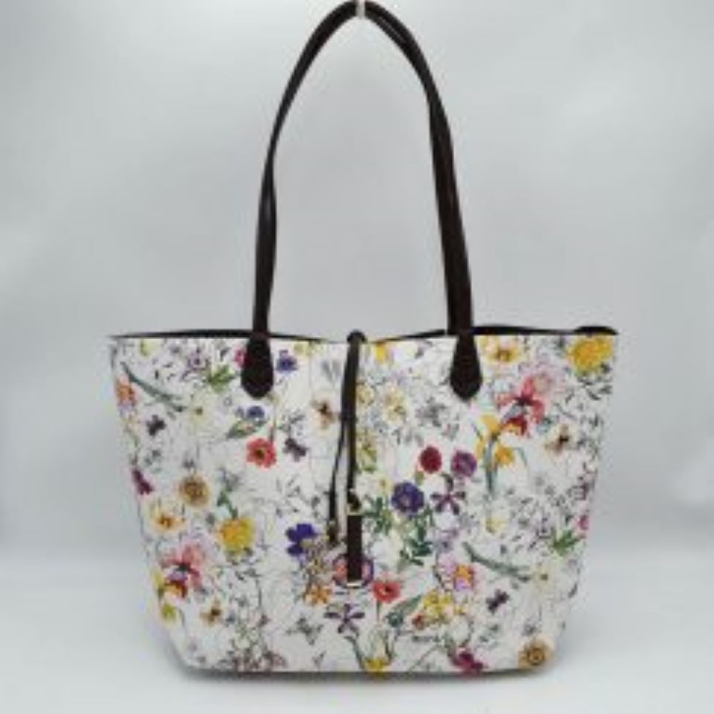Flora This everyday tote bag features an all-over vibrant floral and botanical pattern across its spacious main compartment. Designed for daily use, it is equipped with slim double shoulder straps attached securely to the front and back panels. A central decorative thin tie closure accents the open top design, completing the sleek and functional look.