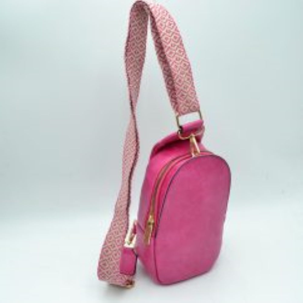 Fuchsial This compact sling backpack features a smooth textured finish and a contoured, teardrop-shaped silhouette designed for casual everyday use. It includes a primary storage compartment that secures with a prominent gold-tone zipper and a flat pull tab for easy access to essentials. A distinctive, wide shoulder strap decorated with an intricate geometric pattern connects via gold-tone metal clips to various anchor loops, allowing for adjustable and versatile cross-body or over-the-shoulder wear.