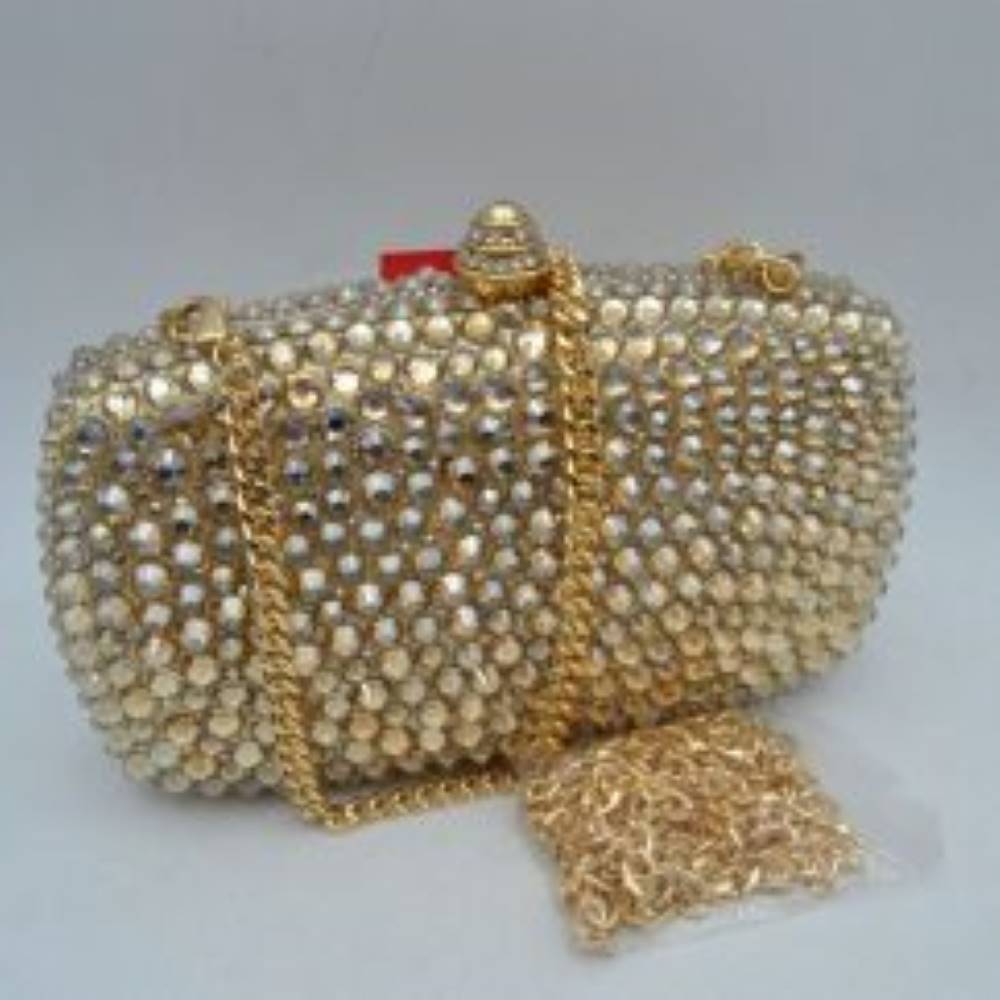 Gold This structured clutch bag features a heavily embellished exterior covered in rows of faceted, multi-dimensional studs that create a textured look suitable for elevated everyday styling or evening events. The compact design opens to a main storage compartment via a secure rigid frame and an ornamental, cylindrical top clasp set with matching small accents. For versatile carrying options, the piece is equipped with a metallic curb chain handle attached to top loop connectors