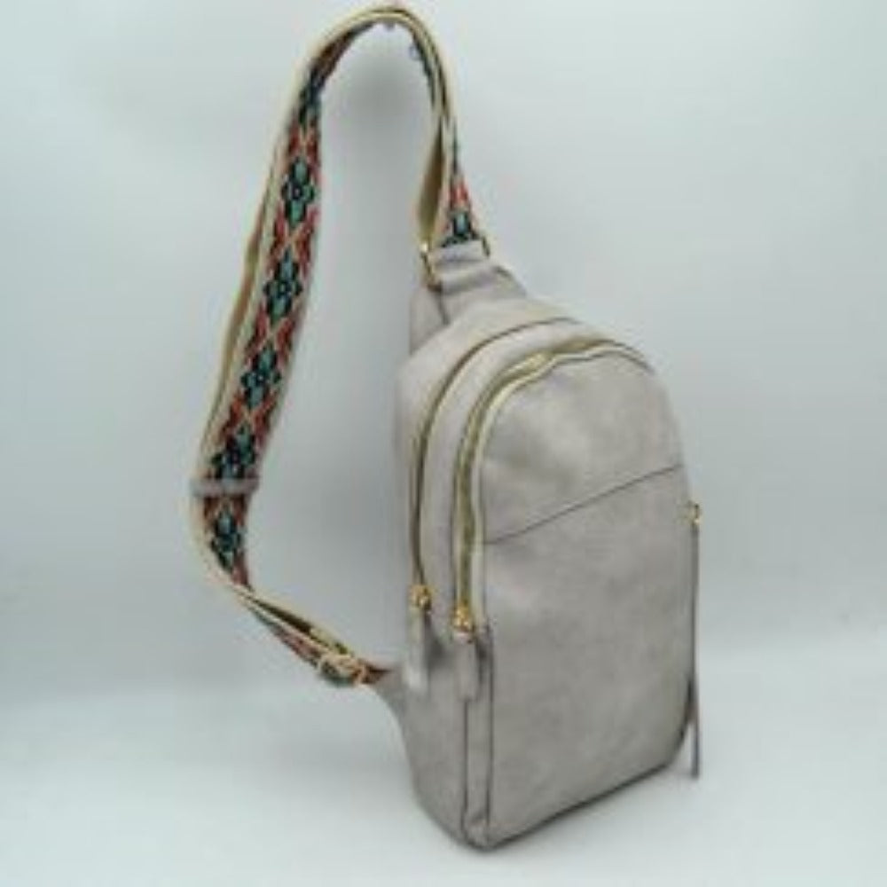 Gray This multi-compartment sling backpack features a smooth texture and a contoured, upright silhouette optimized for daily use. It offers practical storage compartments, consisting of two tiered main sections with independent gold-tone zipper closures alongside a side-access vertical zippered pocket. A distinctive, wide fabric shoulder strap decorated with a detailed geometric woven pattern connects securely to the top and bottom anchors