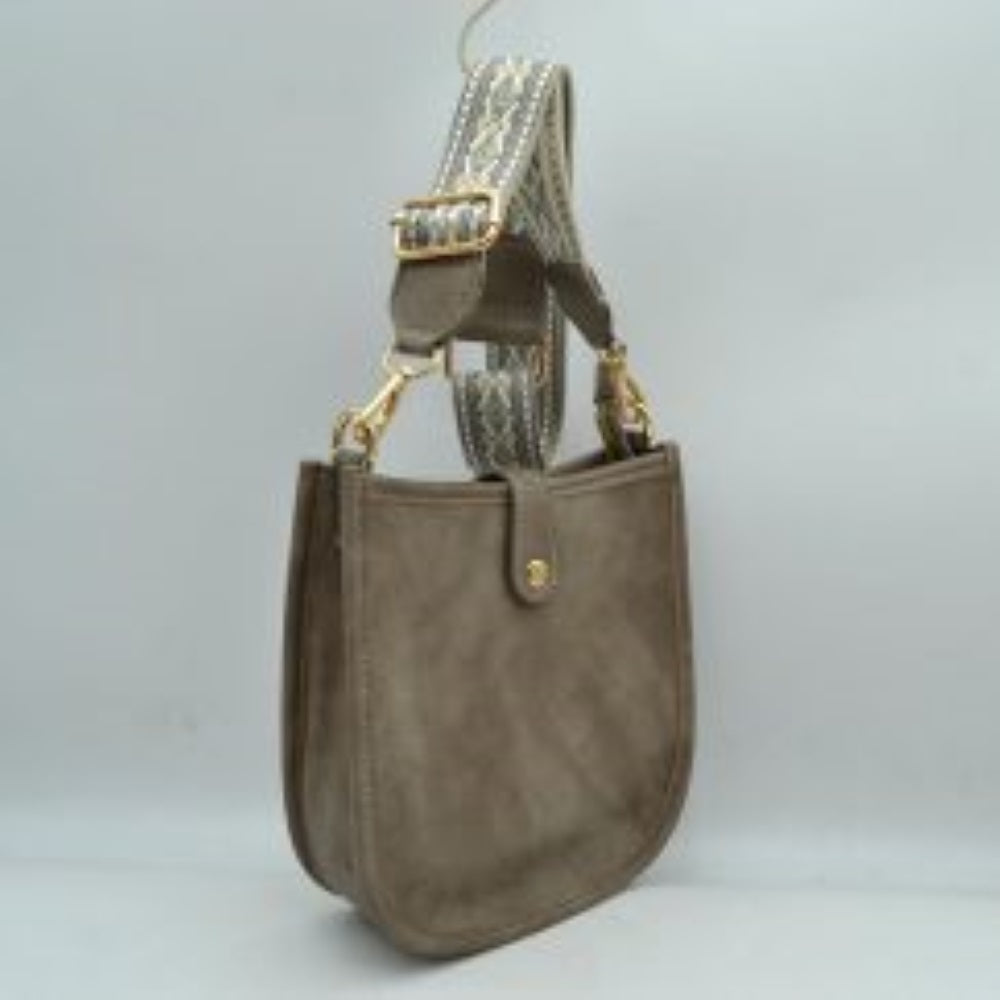 Gray This stylish crossbody bag presents a clean, minimalist design with a smooth exterior finish and a distinct curved, U-shaped silhouette perfect for everyday use. It features an open top main compartment equipped with a small secure tab closure that fastens at the front with a metallic snap button. Adding a striking contrast, the bag is paired with a thick, adjustable fabric strap showcasing a bold geometric pattern