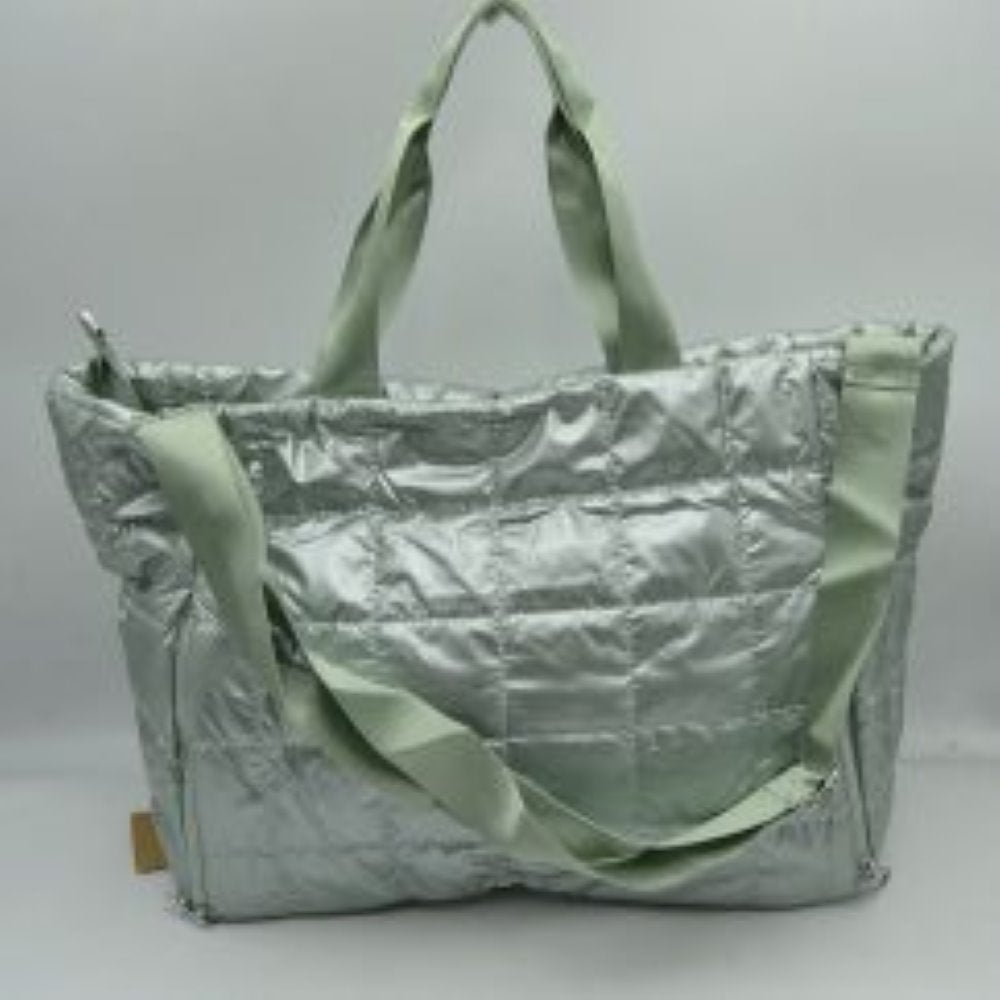 Green Simplify your travel routine with this highly functional, lightweight grid-quilted puffer duffel bag, perfectly proportioned for overnight stays, weekend road trips, or gym days. Featuring a contemporary square quilted design, this soft-structured bag brings an athletic yet polished aesthetic to your transit style. The exterior features two prominent vertical zippered pockets on the lower front corners, keeping your passport, keys, or phone easily accessible while on the move.