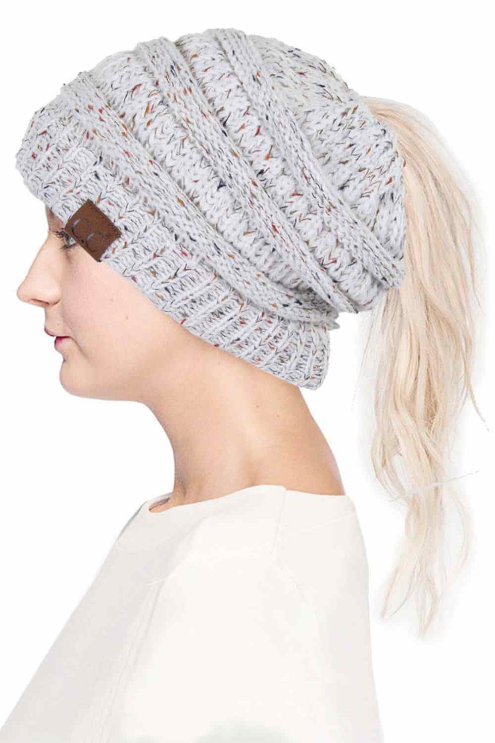 Ivory The C.C Confetti Ponytail Messy Bun Beanie features a soft knit design with subtle confetti flecks for a fun, playful look. Designed with a convenient opening for ponytails or messy buns, it keeps you warm while allowing you to style your hair comfortably.