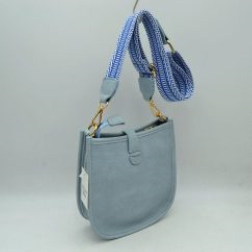 Light blue This stylish crossbody bag presents a clean, minimalist design with a smooth exterior finish and a distinct curved, U-shaped silhouette perfect for everyday use. It features an open top main compartment equipped with a small secure tab closure that fastens at the front with a metallic snap button. Adding a striking contrast, the bag is paired with a thick, adjustable fabric strap showcasing a bold geometric pattern