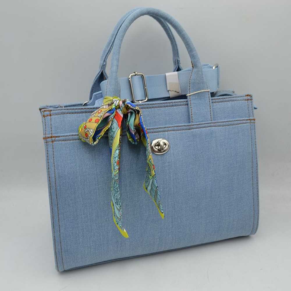 Light Denim Channel effortless casual luxury with this beautifully tailored denim satchel. Combining the timeless, rugged appeal of woven denim with a sharp, structured silhouette, this bag is a standout accessory for your everyday wardrobe. The piece is playfully elevated by a vibrant, multi-patterned twilly scarf knotted at the handle base, adding an instant pop of artistic flair. Whether styled for a casual office setting, a weekend brunch, or a shopping trip, its versatile design ensures you look polish