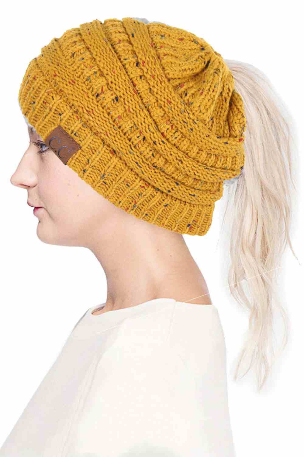 Mustard The C.C Confetti Ponytail Messy Bun Beanie features a soft knit design with subtle confetti flecks for a fun, playful look. Designed with a convenient opening for ponytails or messy buns, it keeps you warm while allowing you to style your hair comfortably.