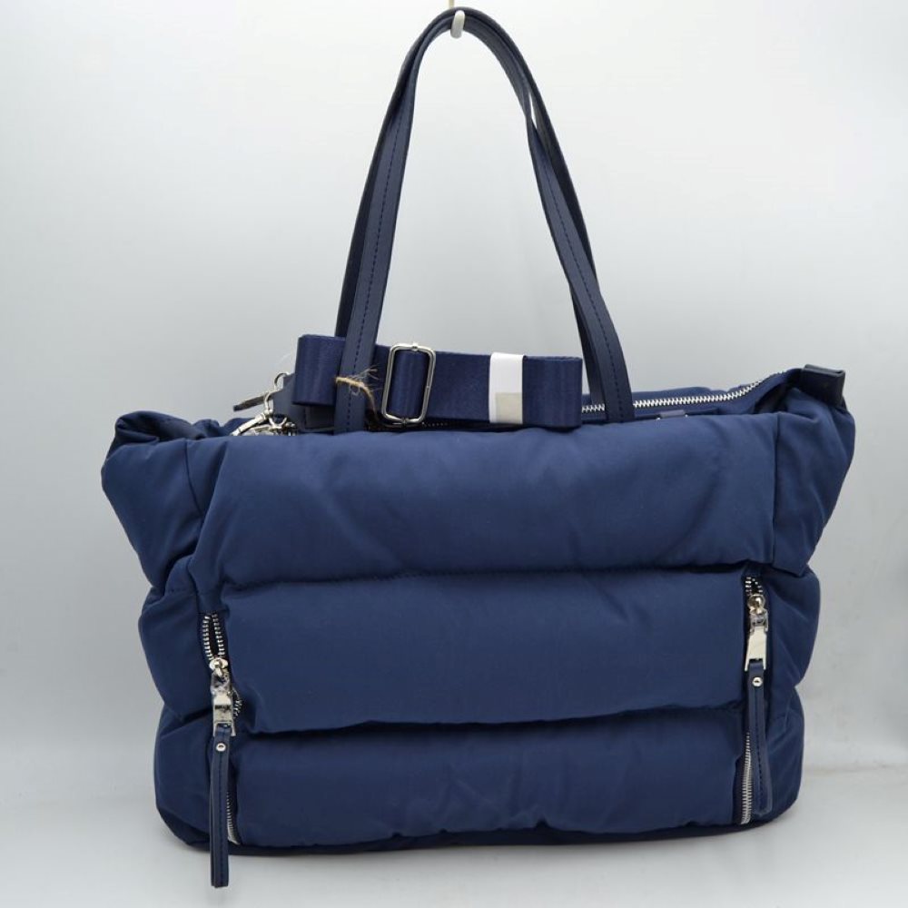 Navy This functional tote bag features a soft, insulated puffer exterior with horizontal quilted channels in a sleek deep navy blue, making it an excellent choice for casual everyday use or travel. Designed for efficient organization, the front is equipped with two vertical side-entry zipper pockets with long fabric pulls for quick access to smaller items. It comes with sturdy flat dual top handles for a comfortable shoulder carry