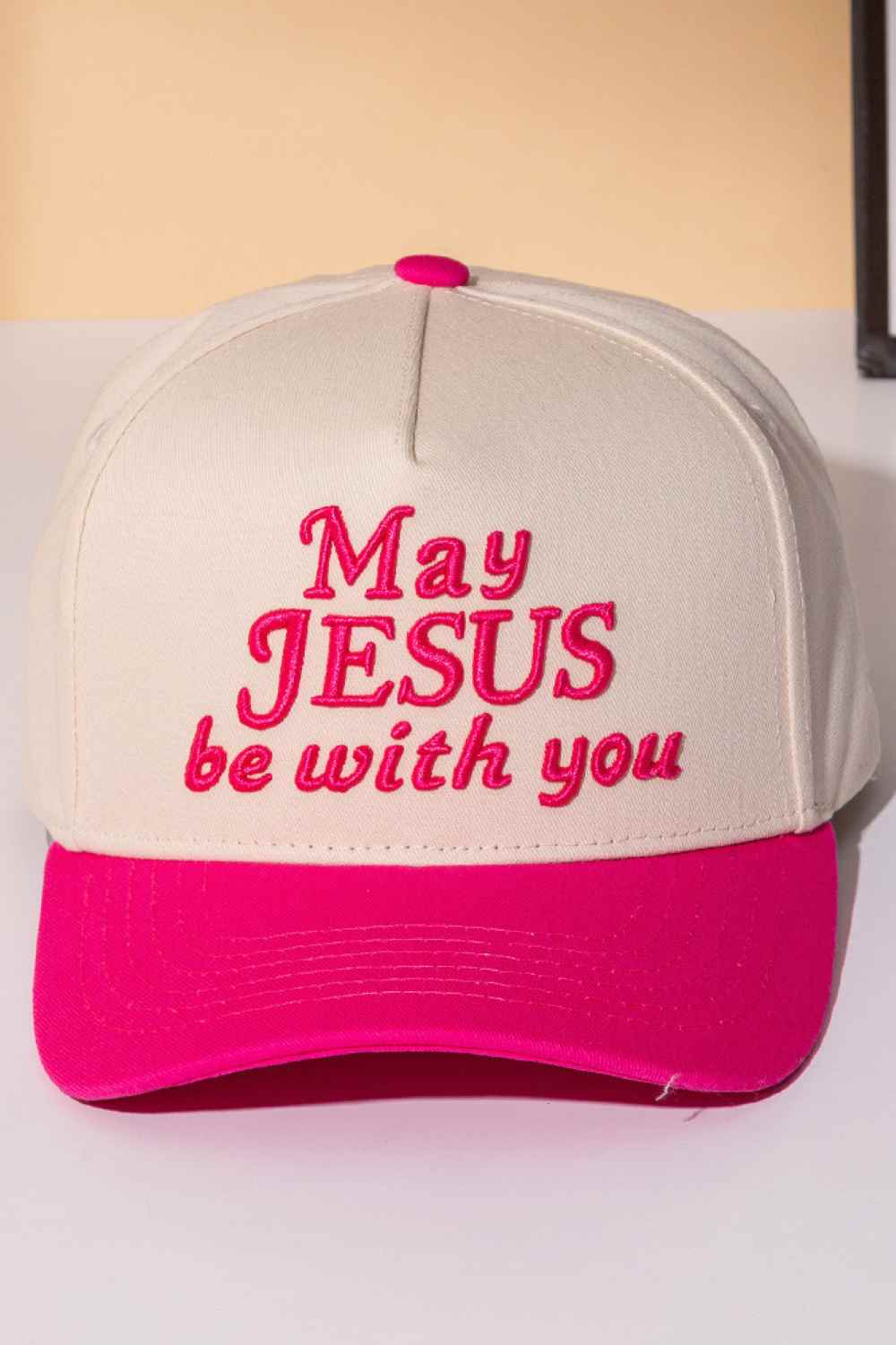 Pink Classic two-tone trucker cap featuring an embroidered "MAY JESUS BE WITH YOU" message across the front. Crafted from 100% cotton for breathability and comfort, this snapback design offers one-size-fits-most versatility. Perfect for everyday wear, outdoor activities, or expressing your faith. The structured six-panel construction and mesh back panels provide durability and ventilation. An ideal accessory for those seeking meaningful style with spiritual significance.