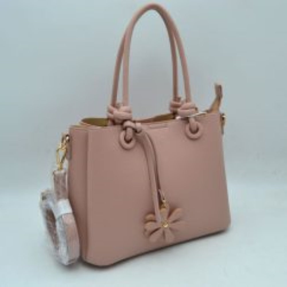 Pink This elegant everyday bag features a textured surface and unique rolled top handles that attach to the body with knotted loop accents. The design offers versatile storage options, highlighting a split-compartment interior with an open side section and a main central area secured by a metallic top zipper. A decorative floral charm hangs from the front handle base, and a detachable, adjustable shoulder strap is connected via metallic lobster clasps to side D-rings