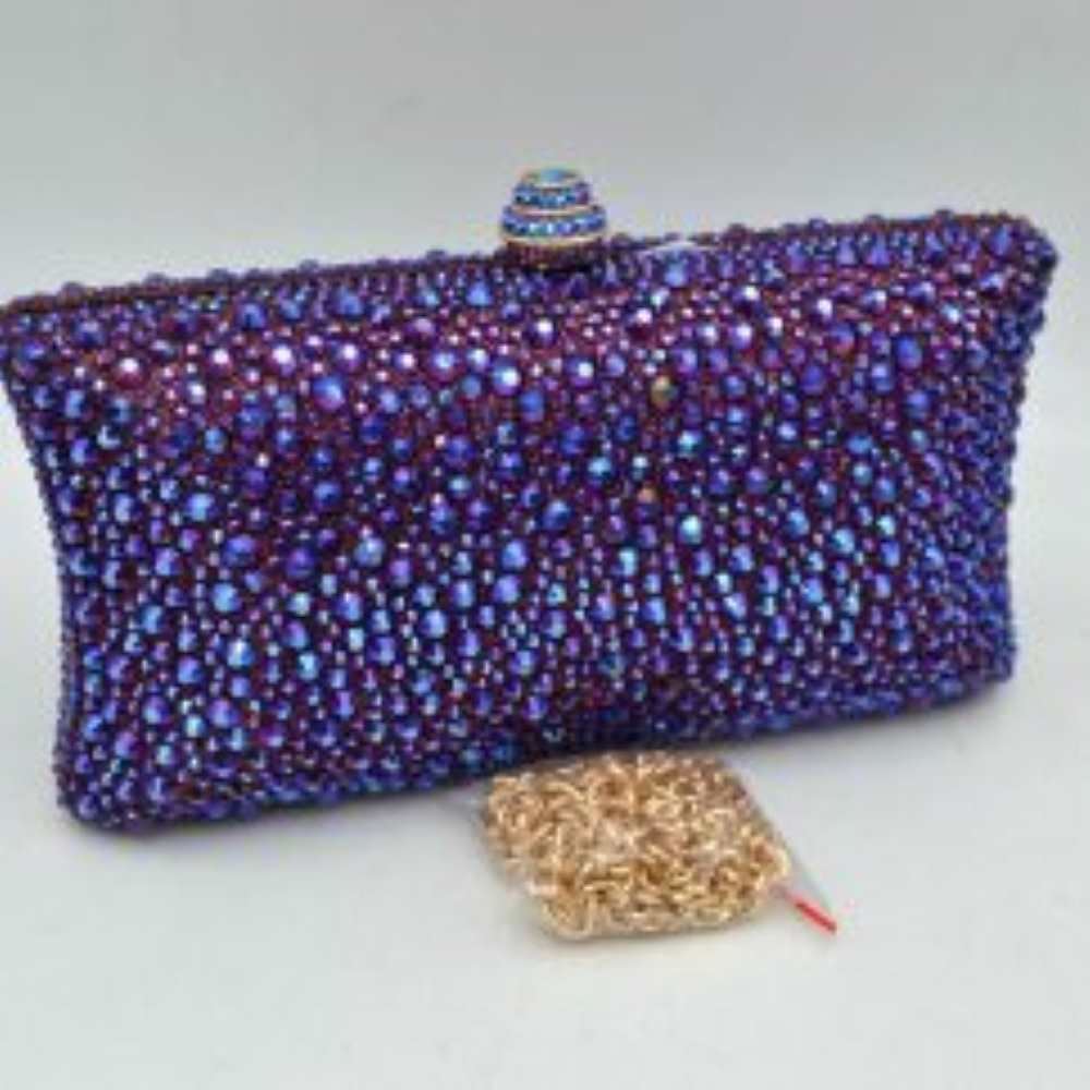 Purple This elegant box clutch bag features an all-over array of faceted, shimmering rhinestone embellishments that fully cover the exterior for a textured, light-catching look. Designed for evening or special occasion use, the structured frame includes a secure top clasp closure with a tiered, decorative knob that easily snaps open to access the main storage compartment. A matching, detachable metallic link chain strap with a secure lobster clasp is included