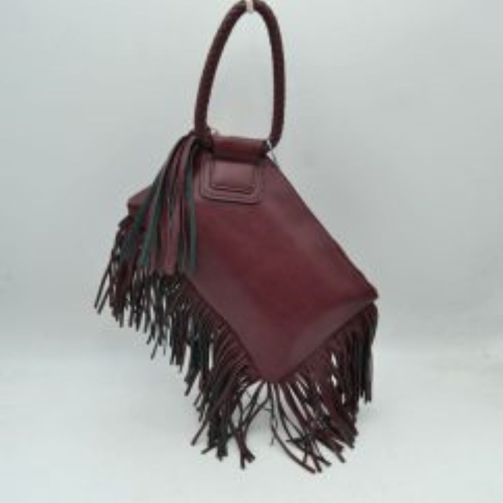 Purple This everyday clutch bag features a smooth, structured body prominently styled with long cascading fringe accents along the lower trim and side panel. Designed for convenient hand carrying, it is equipped with a distinctively braided, circular top handle anchored securely to a reinforced upper flap. The main storage compartment features a secure top zipper closure with metallic teeth